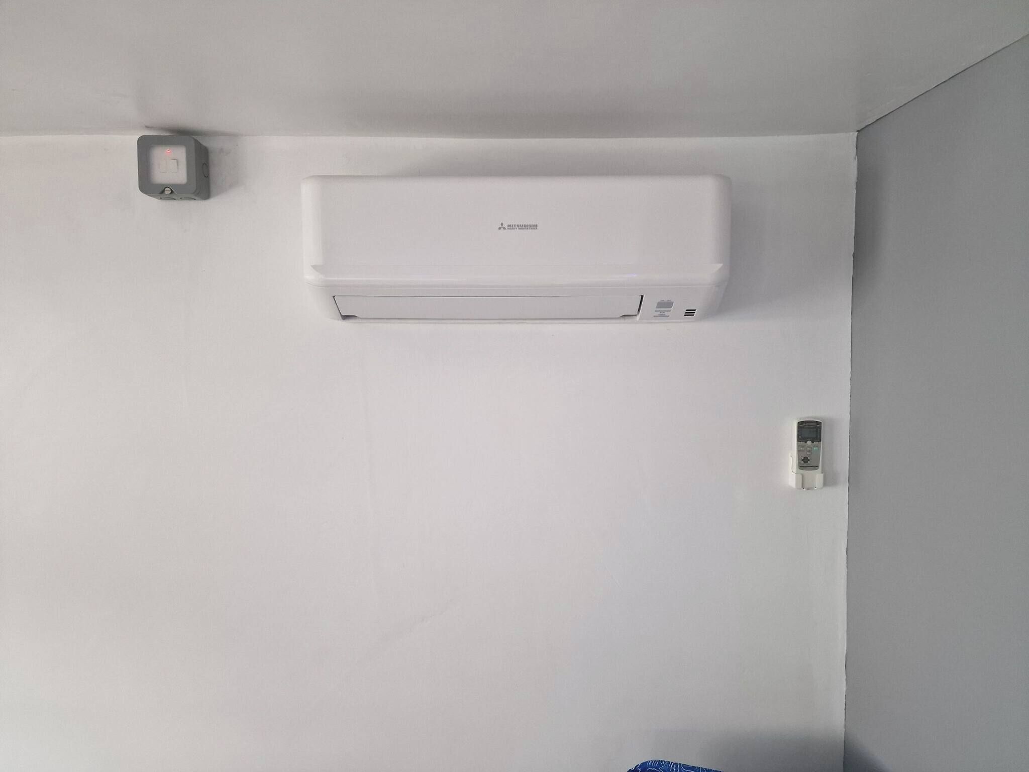 A white air conditioning unit mounted on a plain wall with a small control panel to the left.