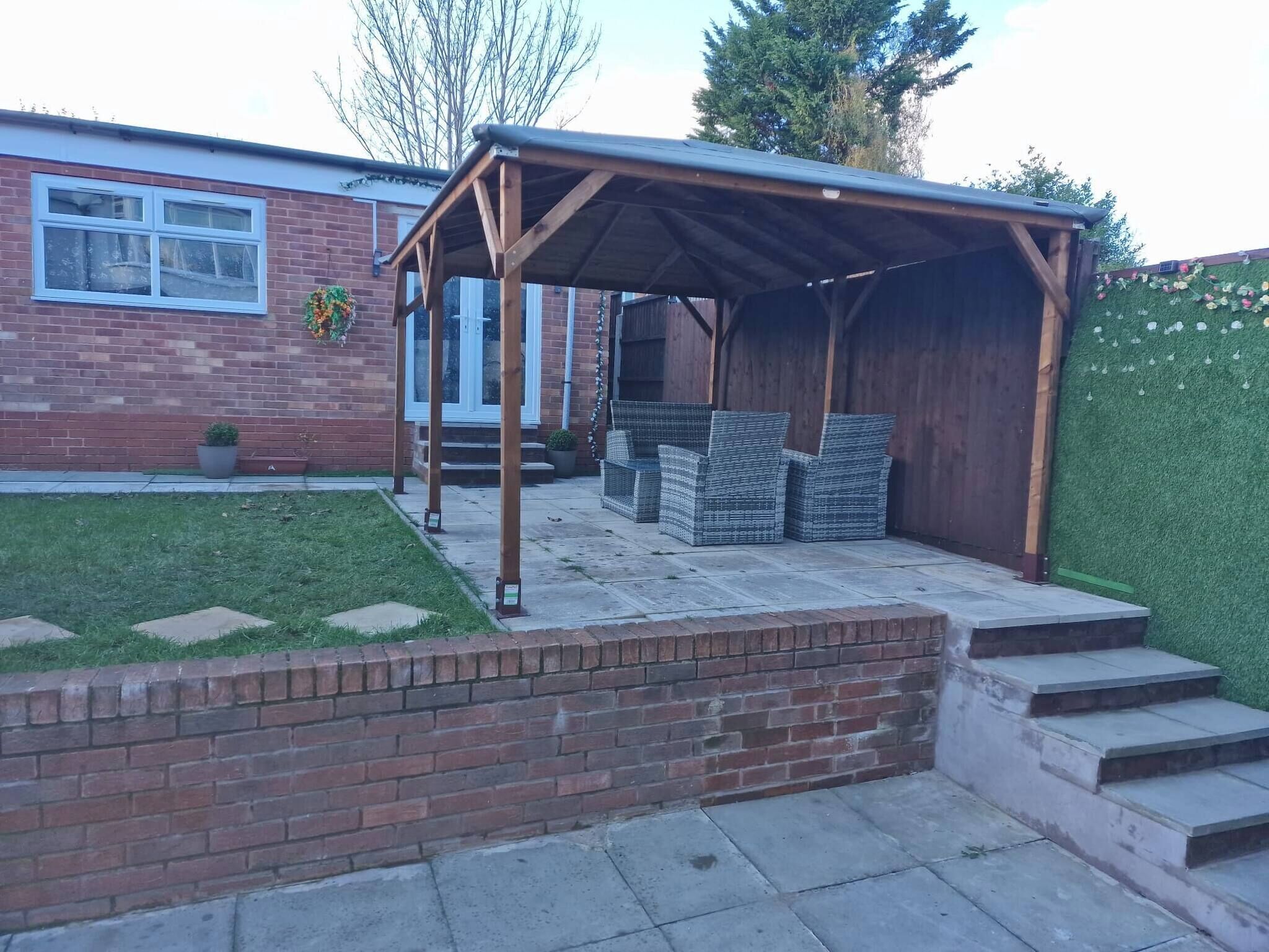 A covered patio area with a brick wall, a wooden pergola, and outdoor furniture.