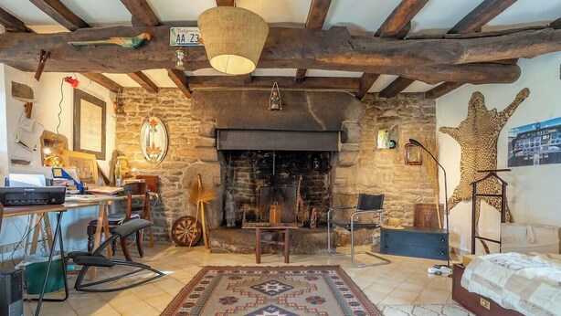 A rustic room with a stone fireplace, wooden beams, a bed, a desk with a computer, and a patterned rug. - Maison bretonne de 1600 : Authenticité & Sérénité (Inzinzac-Lochrist)