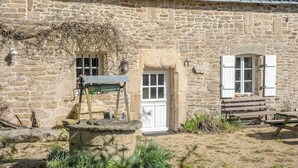 A stone building with a well, a bench, and a small garden area. - Maison bretonne de 1600 : Authenticité & Sérénité (Inzinzac-Lochrist)