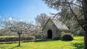 A stone building with an arched entrance, surrounded by a grassy area and trees. - Maison bretonne de 1600 : Authenticité & Sérénité (Inzinzac-Lochrist)