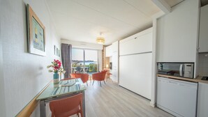 A modern kitchen with white cabinets, a dishwasher, and a microwave. There is a dining area with a glass table and orange chairs. A vase with flowers is on the table. - Sea-view garden-level flat (Ploemeur)