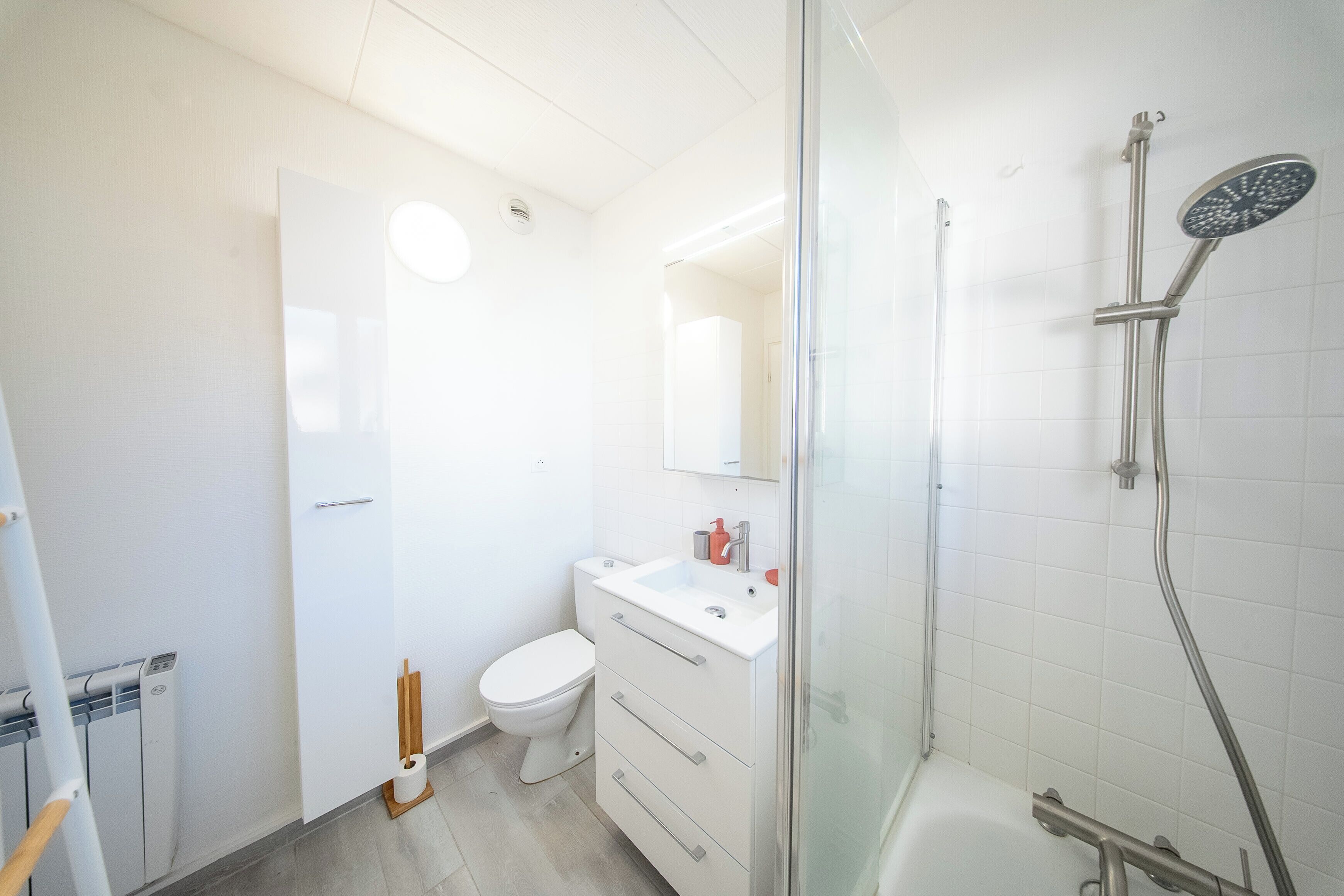 Ein Badezimmer mit Toilette, Waschbecken, Spiegel, Dusche und Glastür.