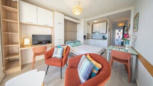 A modern, well-lit room with a bed, a desk with a computer, a TV, and a seating area with chairs. - Sea-view garden-level flat (Ploemeur)