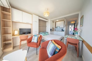 Una habitación moderna y bien iluminada con una cama, un escritorio con computadora, un televisor y una zona de estar con sillones.