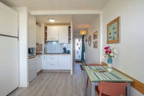 Una cocina compacta con armarios blancos, microondas y cafetera. Hay una mesa de comedor con camino de mesa a rayas y un jarrón con flores.