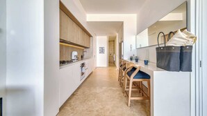 Um corredor estreito com uma cozinha de um lado, cadeiras de madeira, uma mesa e uma bolsa do outro.