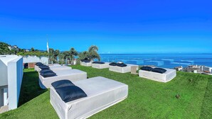 Terraço no telhado com sofás modulares brancos e almofadas pretas, com vista para a paisagem costeira.