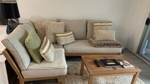 Un soggiorno moderno con un divano beige, diversi cuscini, un tavolino in legno e un telecomando.