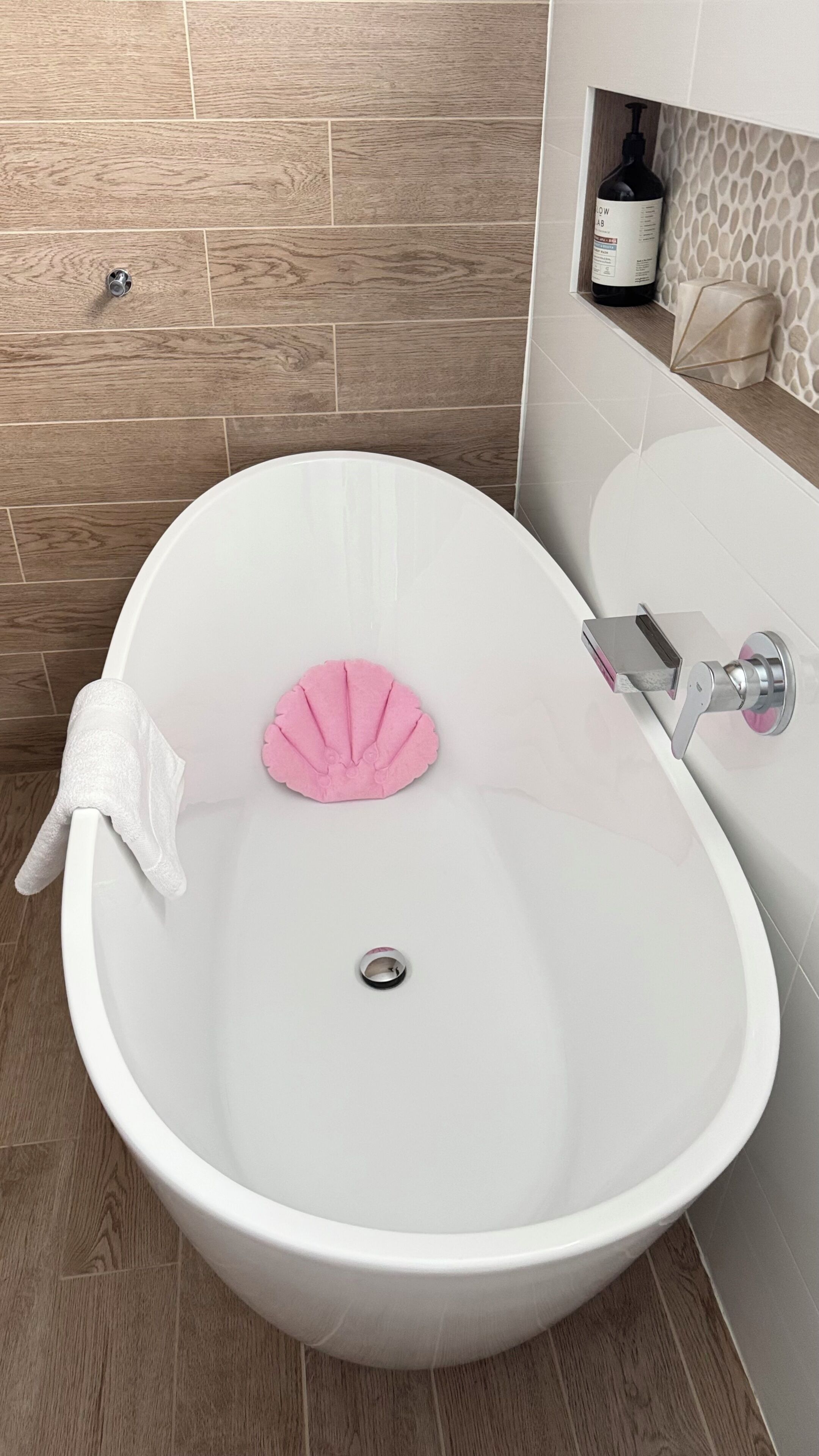 A bathroom with a white bathtub, a pink bath mat, and a bottle of hand soap on the wall.