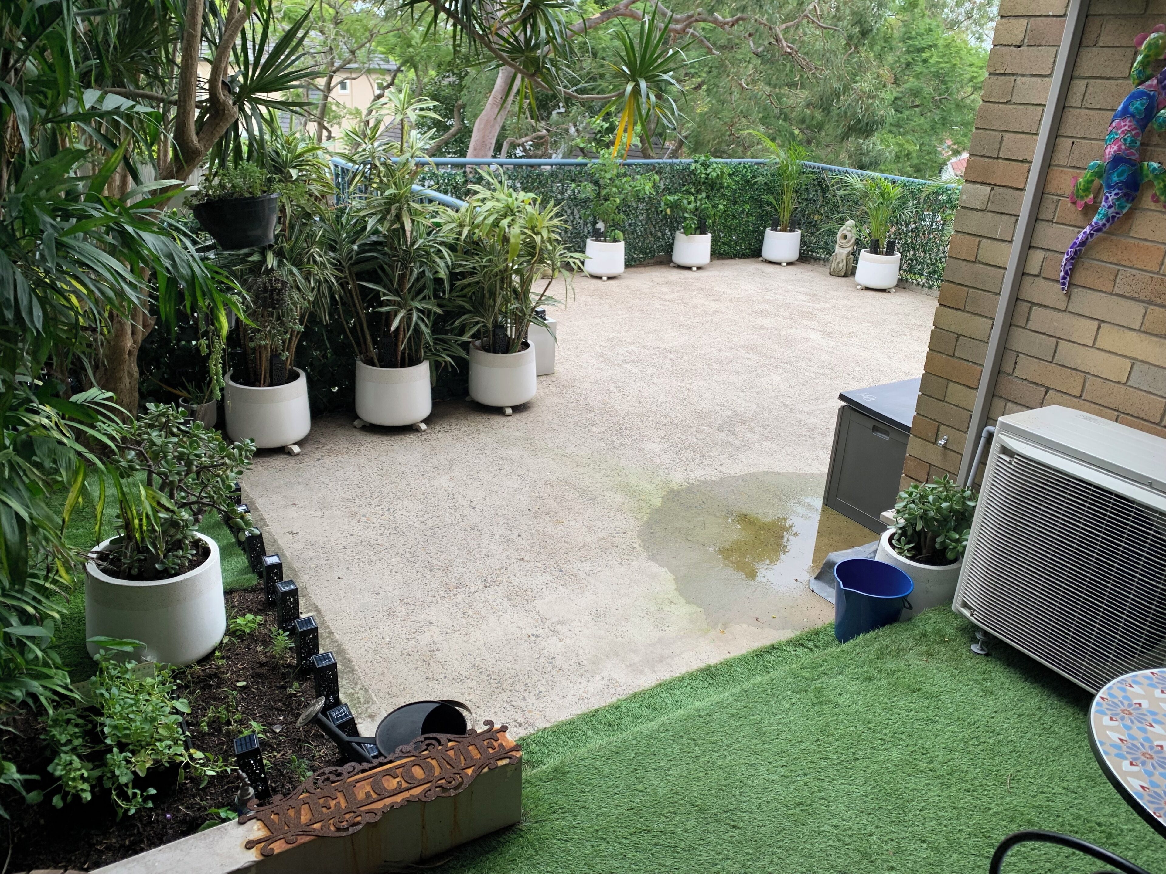 Eine Terrasse mit Blumentöpfen, einem Willkommensschild und einer Klimaanlage.