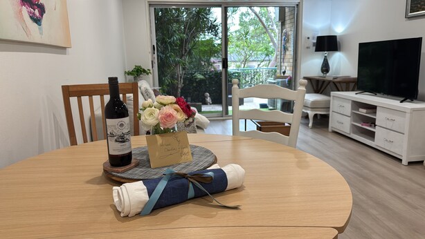 Un tavolo da pranzo con una bottiglia di vino, un biglietto di benvenuto e un asciugamano arrotolato.