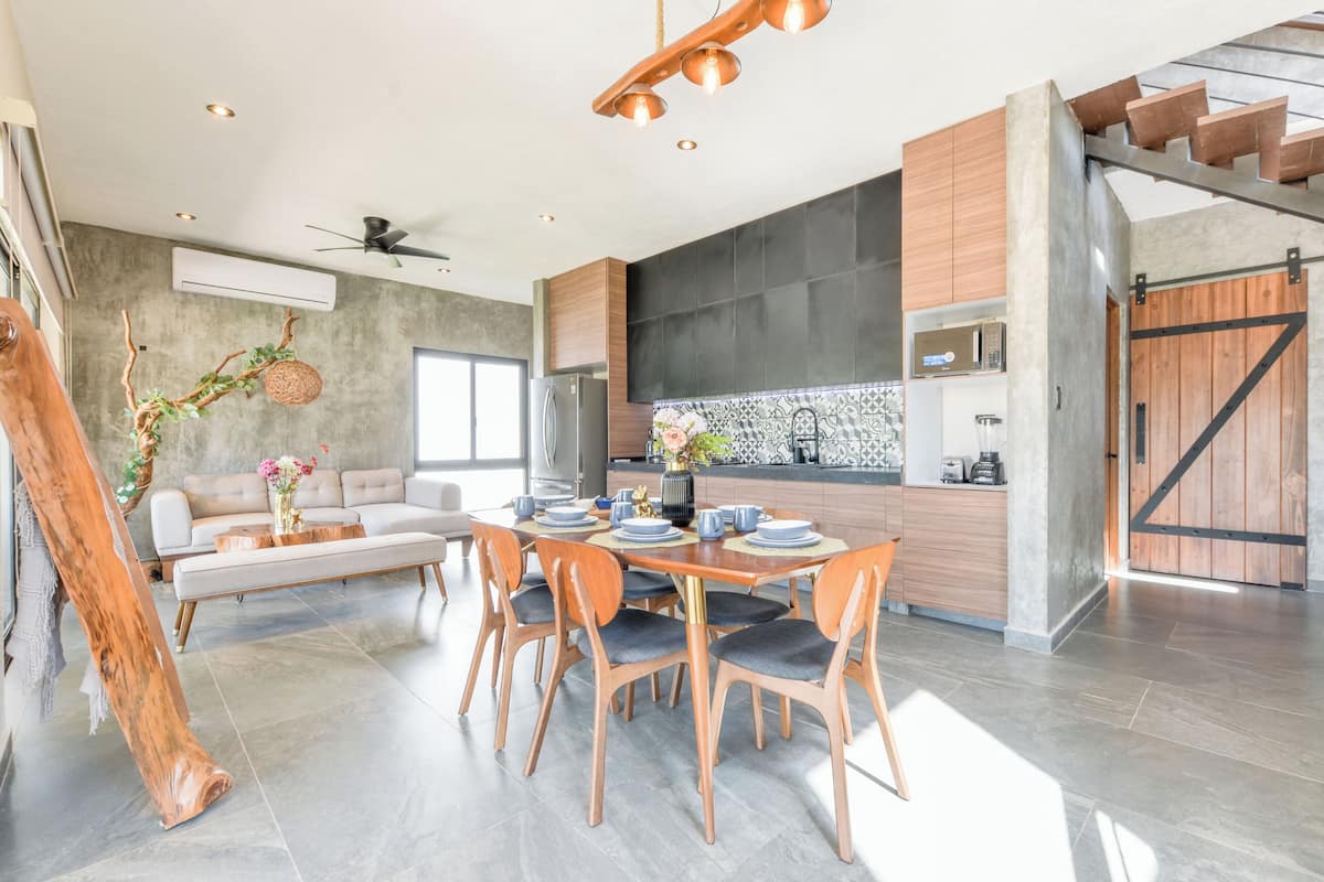 A modern kitchen with a large island, a dining area with a wooden table and chairs, and a staircase leading to an upper level.