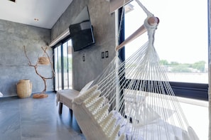 A hammock chair in a modern room with a flat-screen TV mounted on the wall, a large window, and a view of the outdoors.