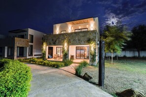 Uma casa moderna de dois andares com fachada de pedra, área de estar externa e entrada bem iluminada.