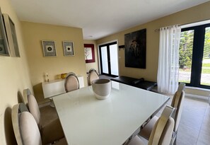 Et spiseområde med et hvidt bord, beige stole, en sort sofa og et billede på væggen.