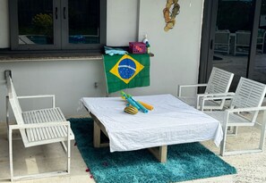 Et værelse med et bord dækket af en hvid dug, to hvide stole, et blå og gult flag og et vindue med udsigt til en pool.