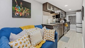 Eine moderne Küche mit Edelstahlgeräten, einem blauen Sofa mit gemusterten Kissen und einem Bild an der Wand.
