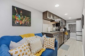 Una cocina moderna con electrodomésticos de acero inoxidable, un sofá azul con cojines estampados y un cuadro en la pared.