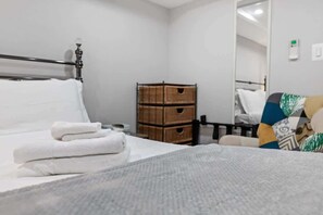 Una cama bien hecha con toallas blancas, un aparador de madera y un espejo en la pared.
