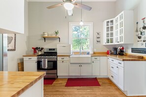 A modern kitchen with white cabinets, a built-in oven, a sink, and a ceiling fan. - Farmhouse | Deck Space | Close to downtown (Wilmington)