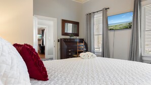 Un dormitorio con cama, cómoda, espejo, televisión y ventana con cortinas.