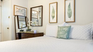 A neatly arranged bedroom with a bed, a dresser, a mirror, and framed artwork on the wall.