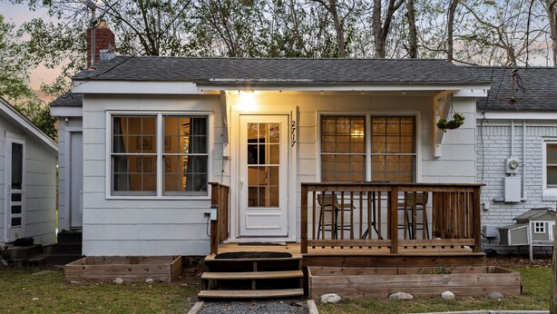 A small white house with a wooden porch, a front door, and a mailbox.