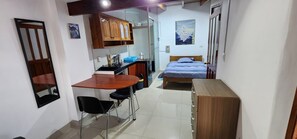 Une pièce de taille modeste comprenant un lit, une petite kitchenette, une table à manger avec des chaises et un miroir.