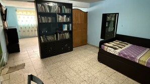 Een slaapkamer met een bed, een boekenkast, een deur en een betegelde vloer.