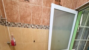 Een badkamer met een geel wastafelmeubel, een handzeepdispenser, een toilet en een glazen deur naar de douche.