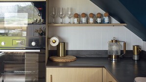 A kitchen with a modern Bosch oven, a coffee maker, and a shelf with wine glasses and jars. - Riverside living, reimagined above the Teifi (Cardigan)