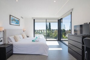 A modern bedroom with a large bed, a TV, and a view of the outdoors. - Villa Karma -Elegant Villa with Pool, Garden & Mul (Benahavís)