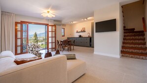 A living room with a sofa, a dining table, and chairs, a kitchen area with cabinets and a TV, and a staircase with ornate railings. - Puebla Aida Unique - Charming Renovated 2 bedroom (Mijas Costa)