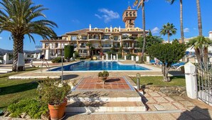 A resort with a swimming pool, palm trees, and a building with a tower. - Puebla Aida Unique - Charming Renovated 2 bedroom (Mijas Costa)