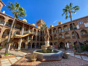 A courtyard with a fountain, palm trees, and a building with multiple balconies and arches. - Puebla Aida Unique - Charming, Renovated 2-Bedroom Apartment (Mijas Costa)