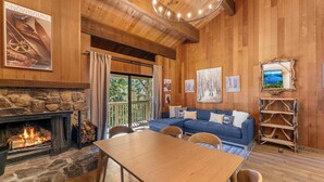 A cozy room with a stone fireplace, wooden ceiling, a blue sofa, and a dining table. - Renovated Condo w/ Pool, Near Lake Tahoe & Beach (Kings Beach)