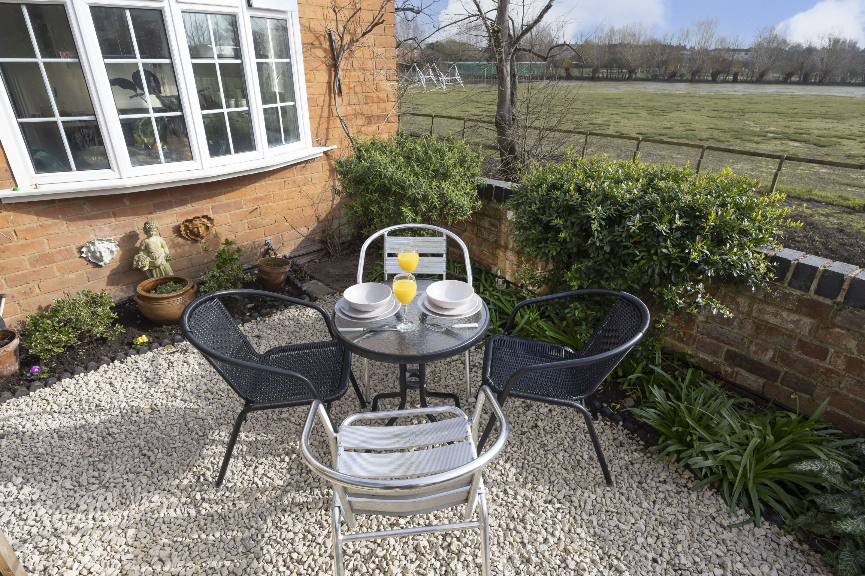 A patio with a table and chairs, surrounded by potted plants and a brick wall.