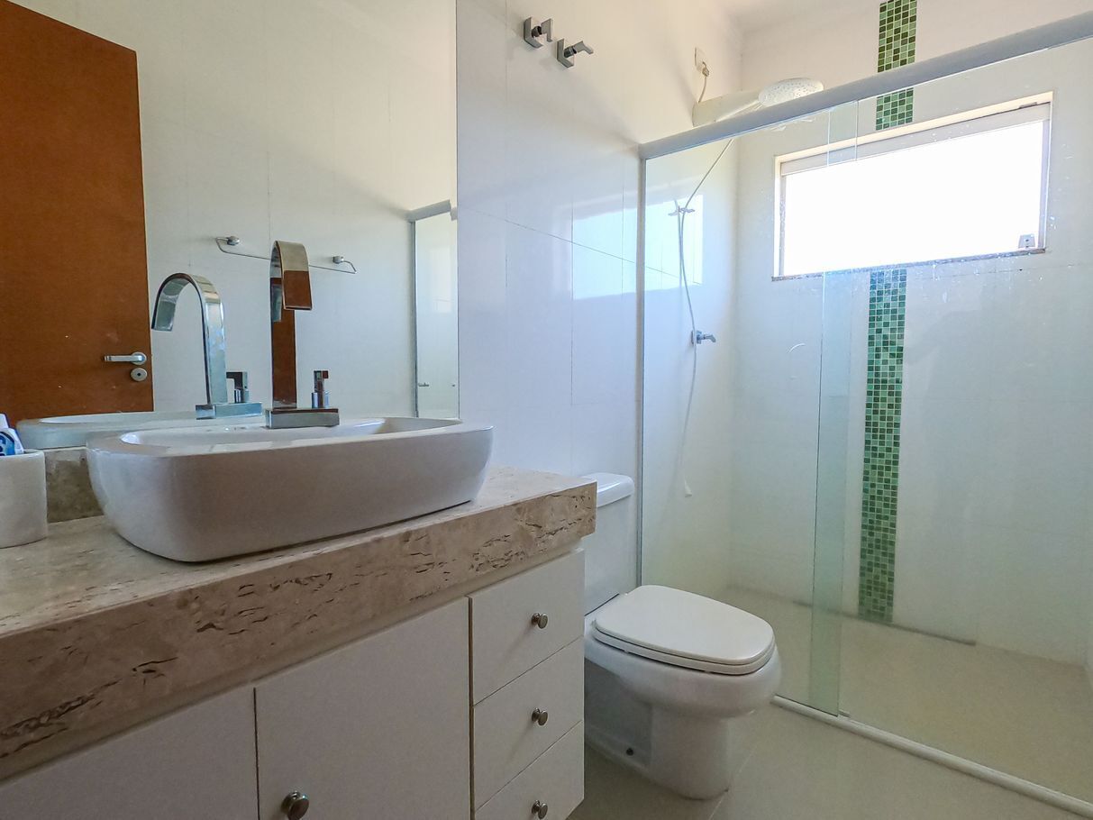 Un baño con lavamanos blanco, inodoro y cabina de ducha con paredes de vidrio.