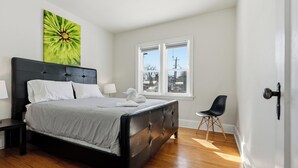 A bedroom with a bed, a chair, a window, and a painting. - Comfortable Crescentwood Bungalow | 3 Bed | 2 Bath | (Winnipeg)