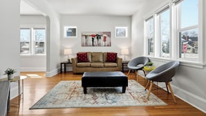 A living room with a sofa, ottoman, chairs, a rug, and artwork on the wall. - Comfortable Crescentwood Bungalow | 3 Bed | 2 Bath | (Winnipeg)
