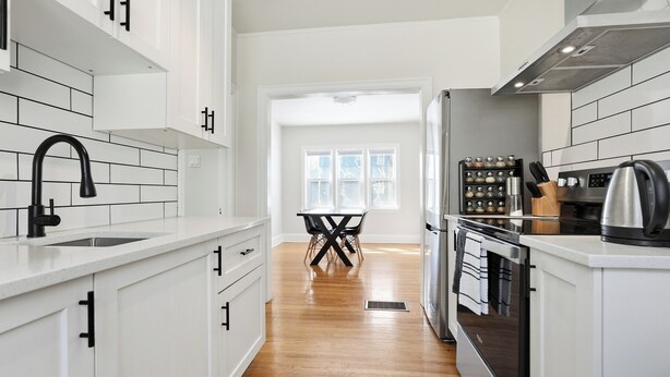 A modern kitchen with white cabinetry, a stainless steel range hood, and a dining area with a table and chairs. - Comfortable Crescentwood Bungalow | 3 Bed | 2 Bath | (Winnipeg)