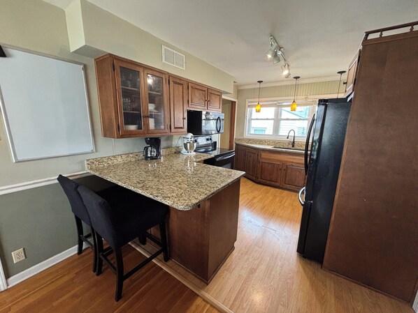A kitchen with granite countertops, wooden cabinets, a black refrigerator, and a coffee maker.