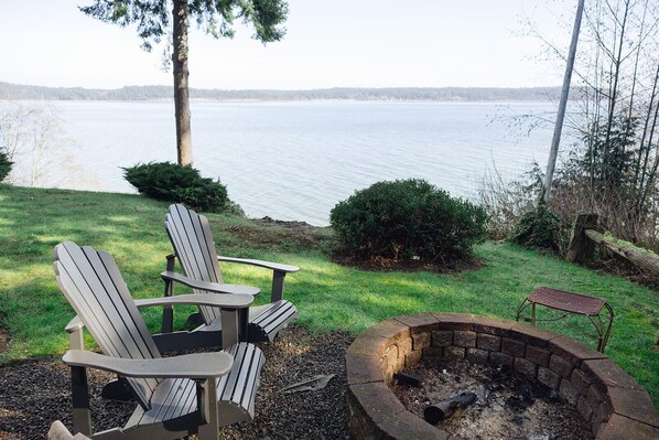 A lakeside outdoor seating area with Adirondack chairs and a fire pit.