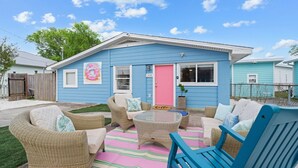 Une maison bleue avec une porte rose, des meubles en osier et un paillasson sur lequel est écrit « Bonjour ».