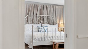 Un cadre de lit en métal blanc, avec une tête de lit, une table de chevet et une lampe.