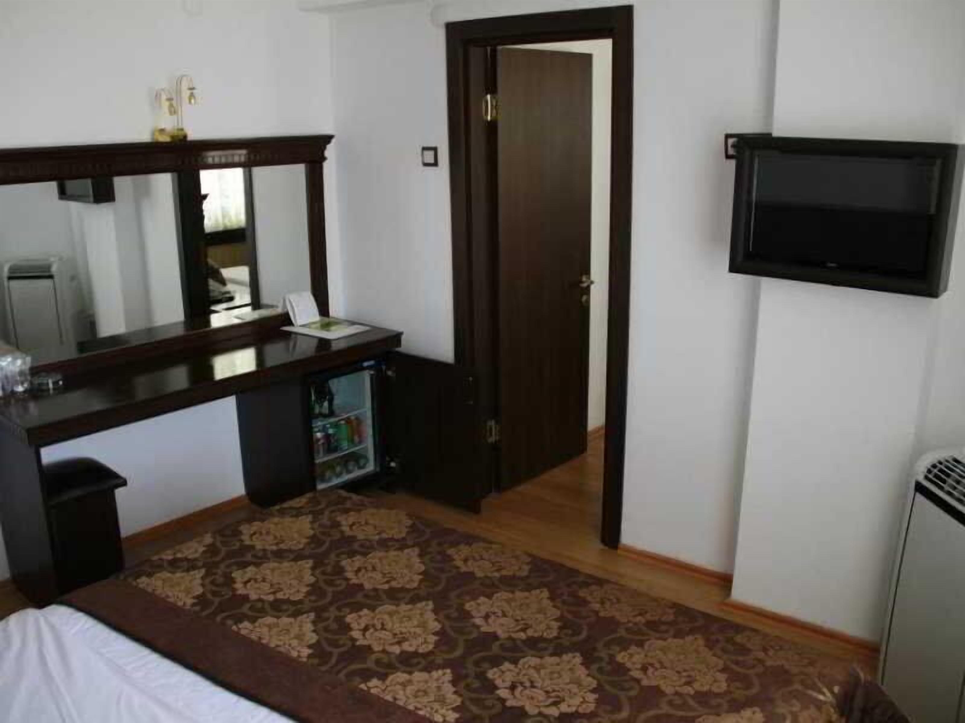 A bedroom with a bed, a desk, a mirror, a television, and a door.