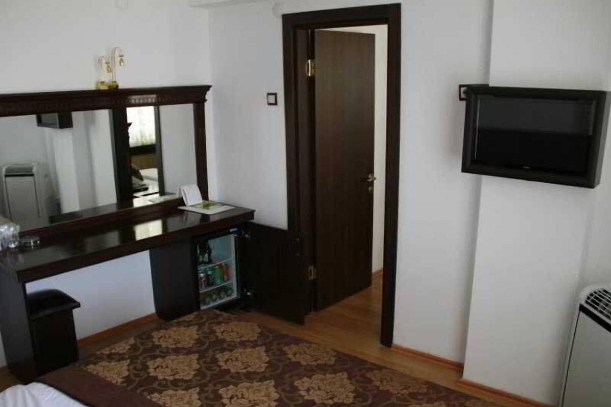 A bedroom with a bed, a desk, a mirror, a television, and a door.