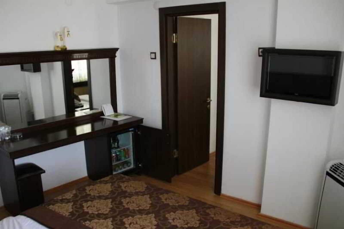 Una camera da letto con un letto, una scrivania, uno specchio, una televisione e una porta.