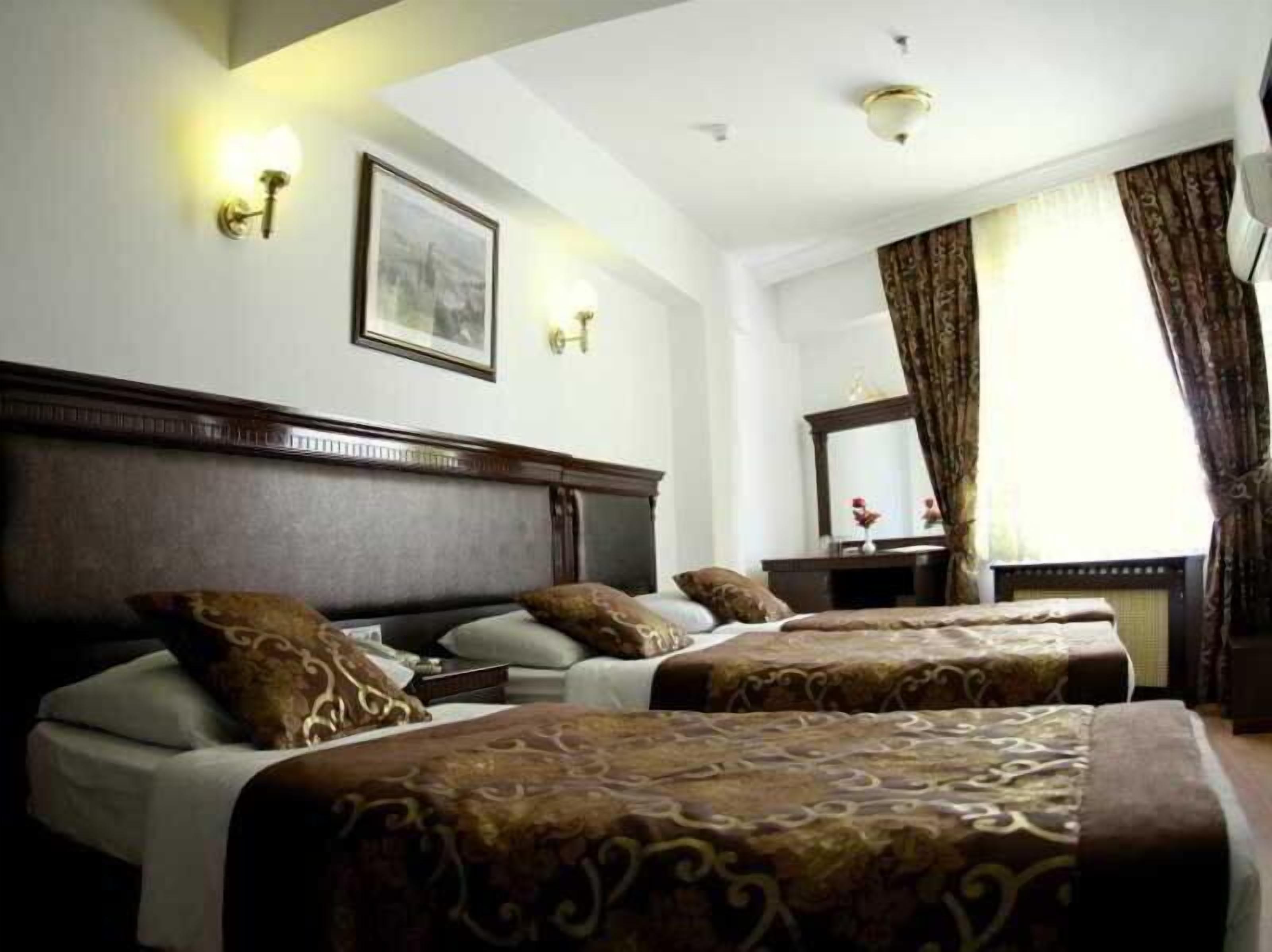 A hotel room with two beds, a wooden headboard, a large mirror, and a window with curtains.